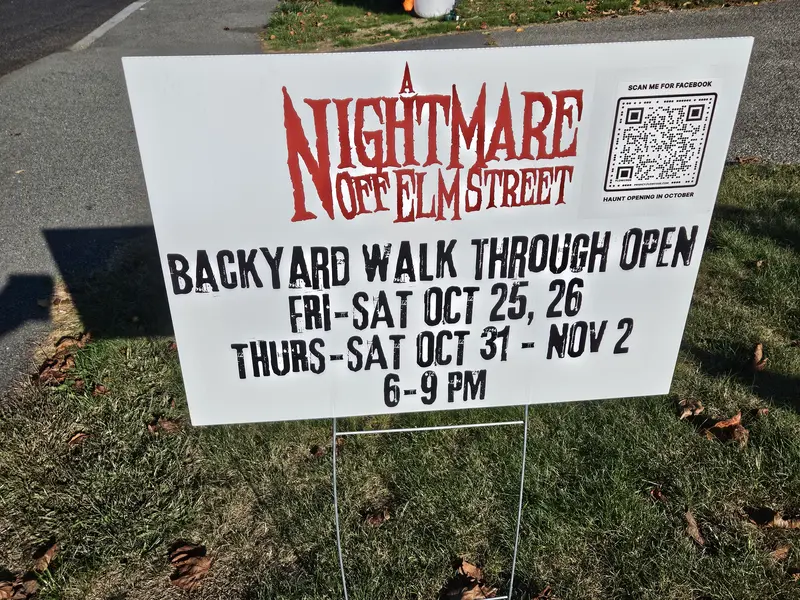 A yard sign advertising 'A Nightmare Off Elm Street' backyard walk-through haunted attraction, featuring dates: Friday-Saturday October 25-26 and Thursday-Saturday October 31-November 2, open 6-9 PM